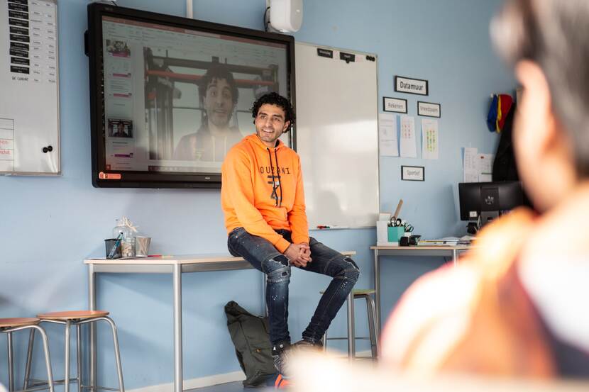 Soufiane Touzani zit op een tafel voor de klas en legt iets uit.