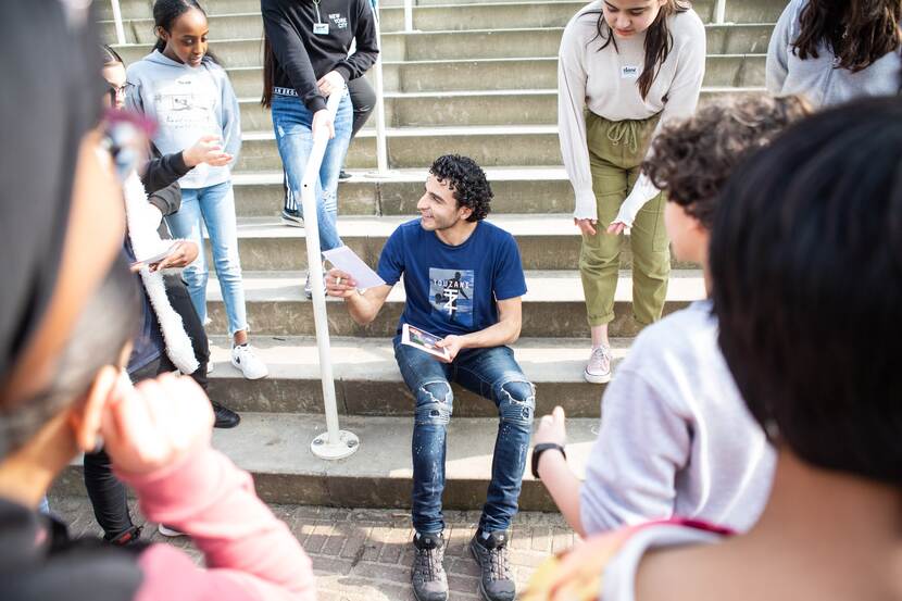 Soufiane Touzani zit op een trap. Hij is in gesprek met kinderen die om hem heen staan.